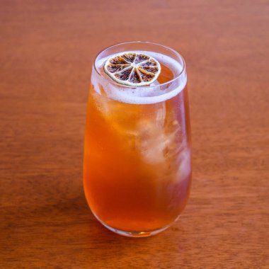 Kurumuş kireç dilimiyle süslenmiş, uzun bir bardak buzlu çay, ahşap bir masada oturur, ferahlatıcı ve davetkar bir atmosfer yaratır.