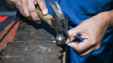 Goldsmith atölyesindeki bir örse çekiçle gümüş bir tel örüyor.