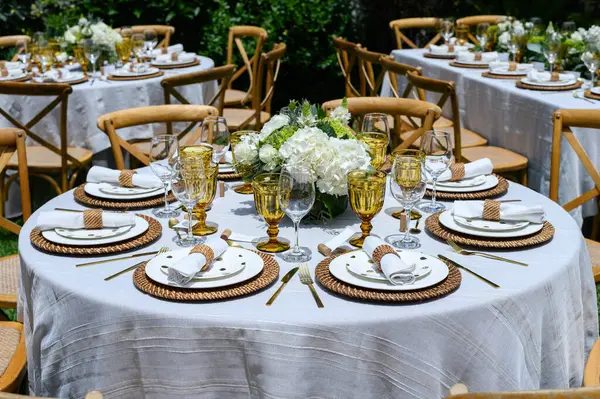 Beyaz masa örtülü yuvarlak masa ve açık hava düğün resepsiyonu için hazırlanan ahşap sandalyeler.