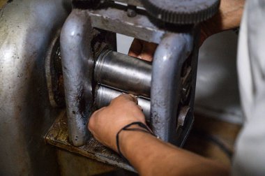 Goldsmith atölyedeki geleneksel bir değirmeni kullanarak bir metal parçası üzerinde çalışıyor.