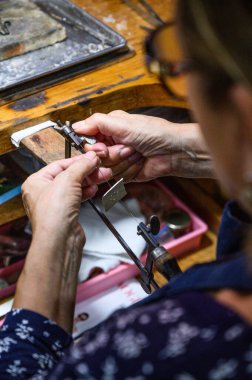 Goldsmith atölyesinde bir testereyle metal bir tabak kesiyor.