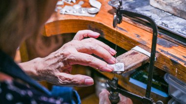 Goldsmith atölyede bir kuyumcuyla gümüş bir tabağı dikkatlice kesiyor.