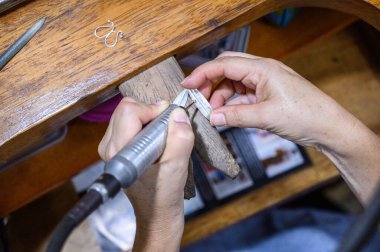 Goldsmith atölyesindeki tezgahta dönen bir aletle gümüş bir mücevher şekillendiriyor.