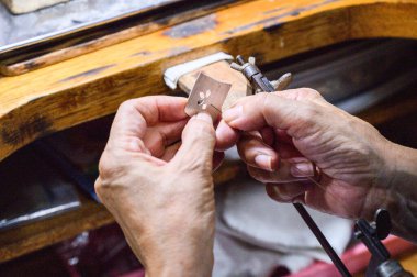 Goldsmith tezgahında bir mücevher üzerinde çalışıyor, demir testeresiyle gümüş bir tabak kesiyor.