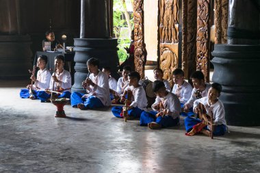 Kültürel giyimli genç Taylandlı müzisyenler sakin bir tapınak ortamında klasik enstrümanlar çalıyorlar.