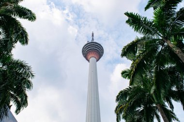 Kuala lumpur kulesi, mavi gökyüzü ve bulutlarla dolu güzel bir günde palmiye ağaçlarıyla çevrili olarak dimdik ayakta duruyor.