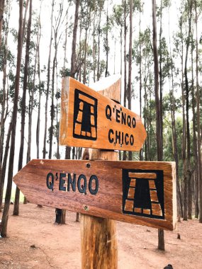 Wooden direction sign indicating the qenqo chico and qenqo inca ruins in cusco, peru, surrounded by tall trees clipart