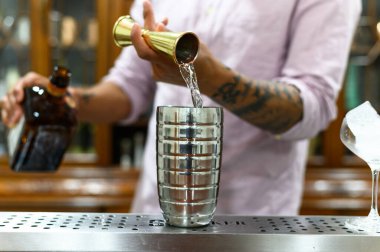 Bir barmen barda ferahlatıcı bir kokteyl hazırlıyor, profesyonel teknikler sergiliyor. İçinde paslanmaz çelik karıştırıcı, dökülen likör ve şık bir bar atmosferi var. Karışım ve içki hazırlama ile ilgili kavramlar için ideal.