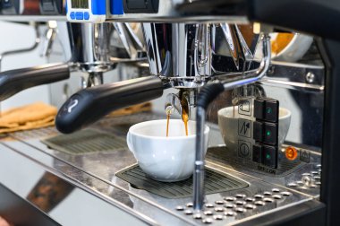 Seramik bir fincanda taze kahve demleyen modern bir espresso makinesinin yüksek çözünürlüklü tasviri profesyonel bir ortamda kaliteli espresso yapma sürecini gözler önüne seriyor..