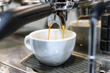 Seramik bir fincanda taze kahve demleyen modern bir espresso makinesinin yüksek çözünürlüklü tasviri profesyonel bir ortamda kaliteli espresso yapma sürecini gözler önüne seriyor..