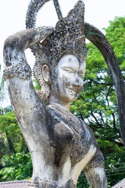 Karmaşık başlıklı yıpranmış heykel, Buda Parkı 'ndaki yemyeşil alanda zarifçe poz veriyor.