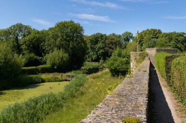 An old stone wall next to a park with a pond, summer, blue sky, Bergues (France)