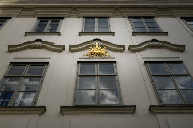 gold decor element of the third eye surrounded by cloud and lightning elements over a big window reflecting clouds of an old high building in Vienna, Austria