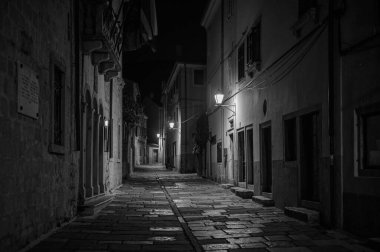 Cres, Hırvatistan - 23 Ekim 2022: Cres 'te gece boyunca eski sokak lambaları olan Dar Sokak, siyah-beyaz