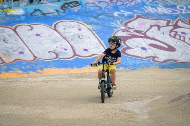 Le Havre, Fransa - 23 Temmuz 2022: Gençler yazın bulutlu bir günde kaykaycı parkında bisiklet süren küçük bir çocuk