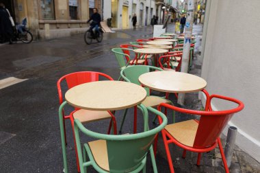 Arles, Fransa - 7 Mart 2023: Renkli Sandalyeler ve sokaktaki bir barın masaları, ilkbaharda yağmurlu bir gün