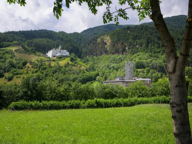 Burgeis, İtalya - 6 Temmuz 2023: Güneşli bir yaz gününde Monte Maria ve Castello del Principe Manastırı, yeşil çayır