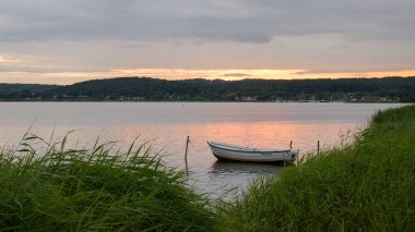 Yazın bulutlu bir günde Ruegen 'de (Almanya) gün doğumu, gölde bir tekne