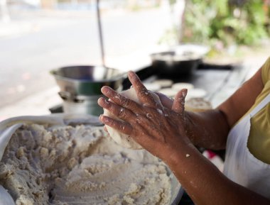 Tanınmayacak kadar yaşlı bir kadın, mütevazı mutfağındaki ızgaranın üstünde elle mısır tortillası hazırlıyor.
