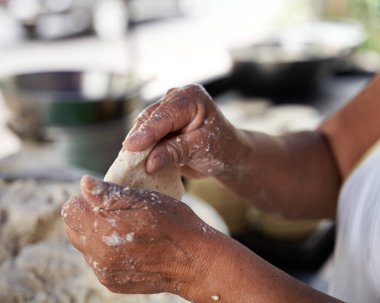Tanınmayacak kadar yaşlı bir kadın, mütevazı mutfağındaki ızgaranın üstünde elle mısır tortillası hazırlıyor.