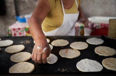 Elleri sıcak ızgarada mısır tortillasını çeviren bir kadın.