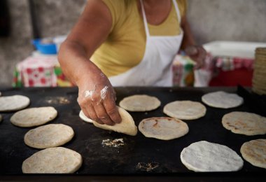 Elleri sıcak ızgarada mısır tortillasını çeviren bir kadın.