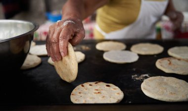 Elleri sıcak ızgarada mısır tortillasını çeviren bir kadın.