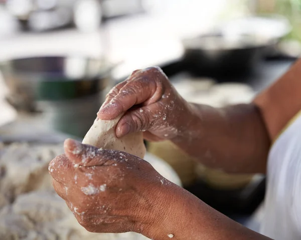 Tanınmayacak kadar yaşlı bir kadın, mütevazı mutfağındaki ızgaranın üstünde elle mısır tortillası hazırlıyor.