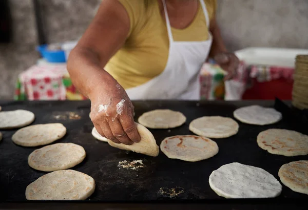 Elleri sıcak ızgarada mısır tortillasını çeviren bir kadın.