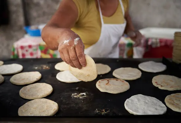 Elleri sıcak ızgarada mısır tortillasını çeviren bir kadın.