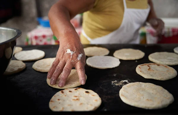 Elleri sıcak ızgarada mısır tortillasını çeviren bir kadın.