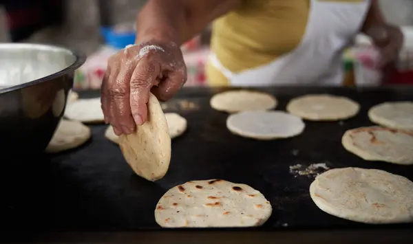 Elleri sıcak ızgarada mısır tortillasını çeviren bir kadın.