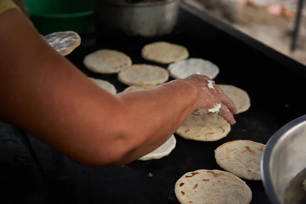 Elleri sıcak ızgarada mısır tortillasını çeviren bir kadın.