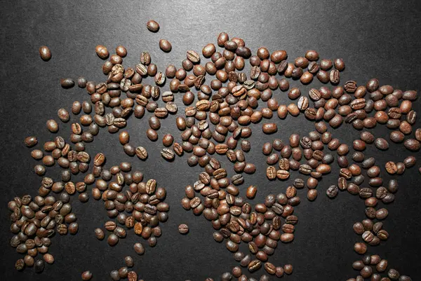 Roasted coffee beans lie across the frame on a black surface with a glare of light. Photo view from above.