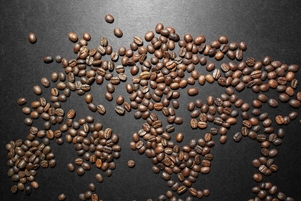 Roasted coffee beans lie across the frame on a black surface with a glare of light. Photo view from above.