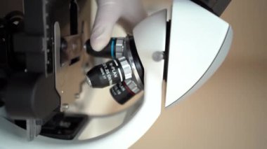 Laboratuvar teknisyeni mikroskobu ayarlıyor. Dikey video. Yakın plan. Mikroskopla çalışan laboratuvar teknisyeni. Laboratuvarda modern mikroskop