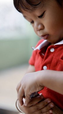 Yüzünün yakın plan fotoğrafı, taşıdığı oyuncakla ilgilenirken Asyalı bebek ciddi görünüyor.