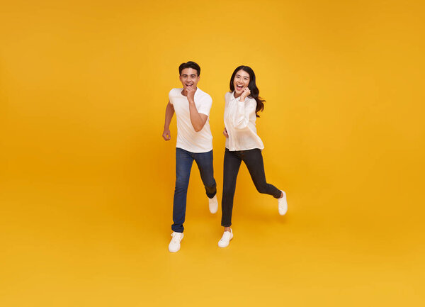 Full length funny sweet asian couple dressed white t-shirt running jumping isolated yellow color background.