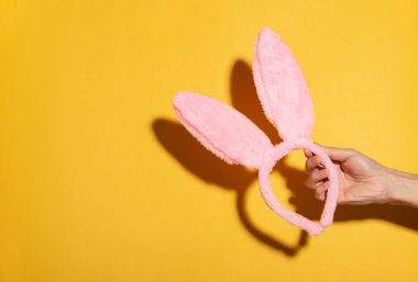 Happy easter, hand holding pink bunny ears on yellow background. decoration in holiday. copy space.