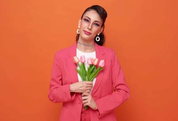 International Women\'s Day. Extremely happy woman in pink clothes she is holding tulip flowers in her hands isolated on studio background.