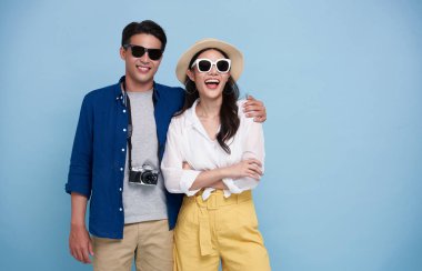 Excited Asian couple tourist dressed in summer clothes to travel on holidays isolated on blue background.
