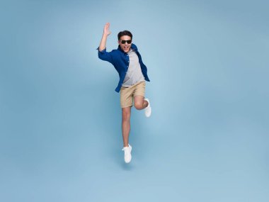 Full lenght portrait of smiling handsome Asian man jumping isolated on blue studio background.
