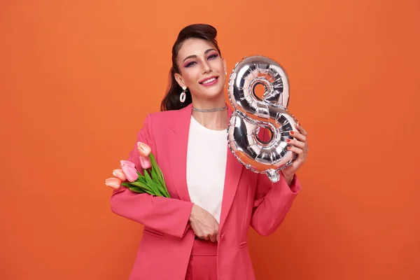 International Women\'s Day. Extremely happy woman in pink clothes she is holding tulip flowers and number 8 in her hands isolated on studio background.