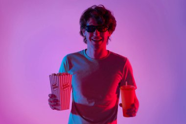 3 boyutlu gözlük takan genç adam patlamış mısır yemekten ve neon ışıklarla film izlemekten zevk alıyor..