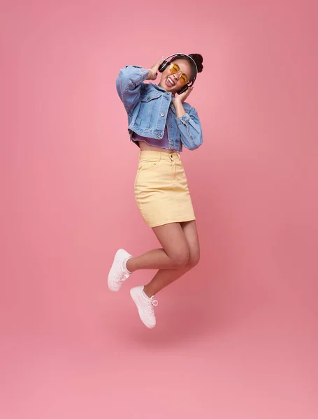 ピンクの背景のスタジオの肖像画に孤立ジャンプ面白い若いアジアの女性 ヘッドフォンで音楽を聴き 人々のライフスタイルコンセプト — ストック写真