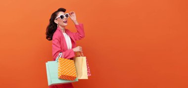 Mutlu gülümseyen moda kadın alışveriş çantaları taşıyor ve alışveriş promosyonu arıyor turuncu arka planda izole edilmiş yaz indirimi.