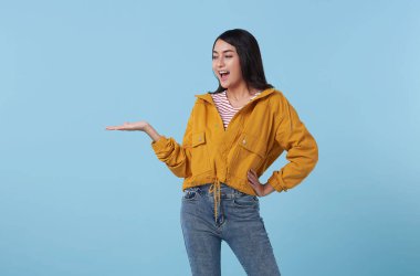 Mavi arka planda izole edilmiş ürün için açık avuç içi fotokopi alanı sunan veya gösteren mutlu Asyalı kadın