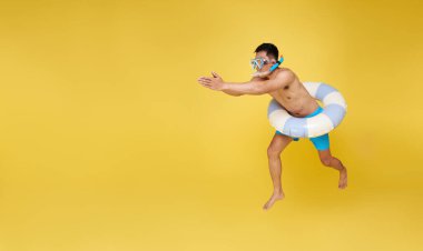Yüzen şnorkel ve şişme yüzükle atlayan neşeli, genç bir adamın tam boy portresi sarı fotokopi arkaplanda izole bir şekilde eğleniyor..