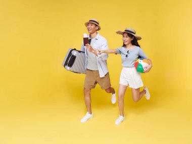 Mutlu Asyalı çift seyahat eden elleri, sarı arka planda izole edilmiş tatillerde seyahat etmek için bavullarıyla birlikte kopyalama alanını işaret ediyor..