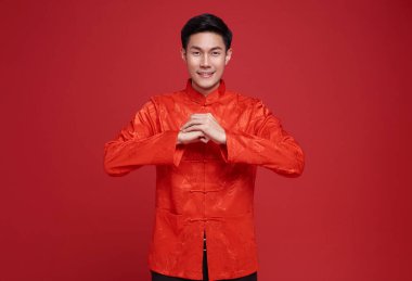 Yeni Çin yılın kutlu olsun. Kırmızı elbiseli Asyalı adam kırmızı arka planda izole edilmiş tebrik işareti yapıyor..